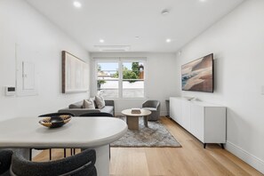 A modern living room with a dining area, a sofa set, a coffee table, and a large window with a view of a house.