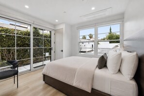 Un dormitorio con una cama grande, una puerta de cristal que da a un balcón y una ventana con vistas a edificios.