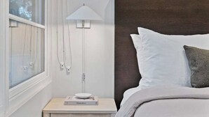 Een slaapkamer met een bed, een nachtkastje met een lamp en een raam.