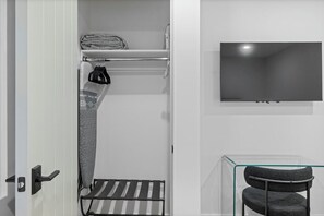 A modern bathroom with a towel rack, a shower area, a glass-enclosed chair, and a mounted TV.