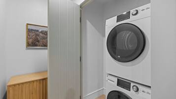 Une buanderie équipée d’un lave-linge et d’un sèche-linge, d’une armoire en bois et d’un tableau encadré accroché au mur.