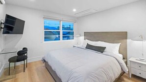 Une chambre moderne avec un grand lit, un téléviseur fixé au mur, une fenêtre donnant sur un beau paysage et une table de chevet avec une lampe.