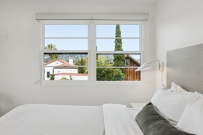 A bedroom with a bed, a window, and a view of a house and trees.