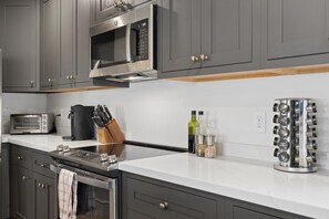 A modern kitchen with grey cabinets, a built-in oven, a microwave, a coffee maker, and a spice rack.