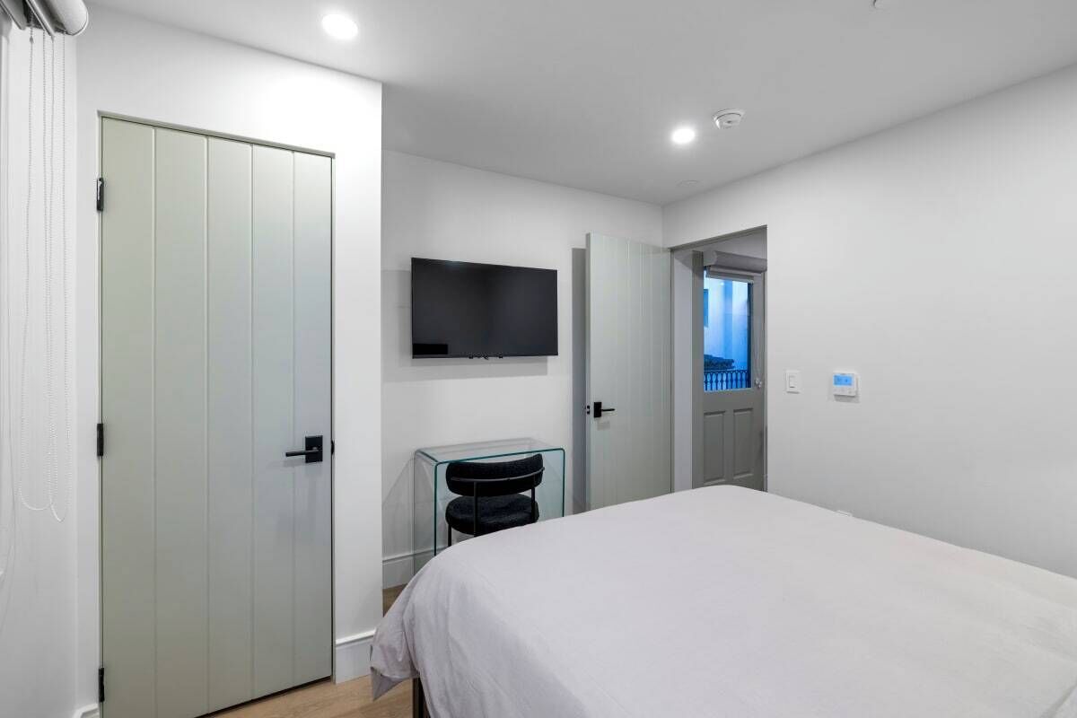 Une chambre d’hôtel moderne, équipée d’un lit, d’un téléviseur fixé au mur et d’une porte donnant sur une autre pièce.