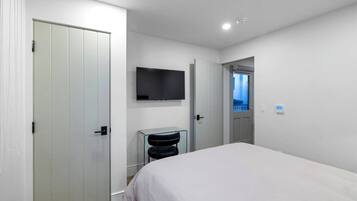 Une chambre d’hôtel moderne, équipée d’un lit, d’un téléviseur fixé au mur et d’une porte donnant sur une autre pièce.