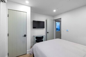 A modern hotel room with a bed, a TV mounted on the wall, and a door leading to another room.