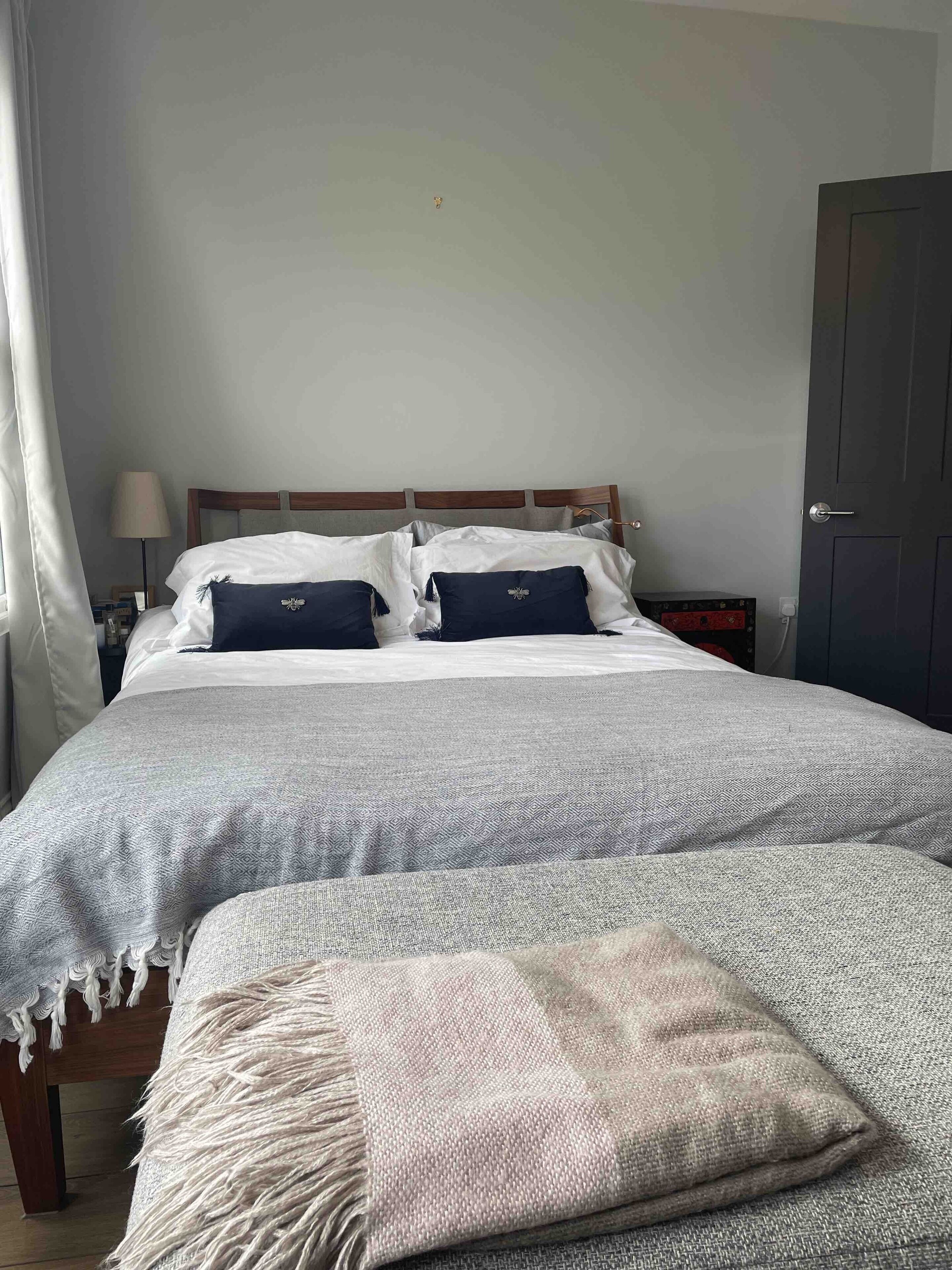 A neatly made bed with a patterned bedspread and pillows, a bedside table with a lamp, and a door in the background.