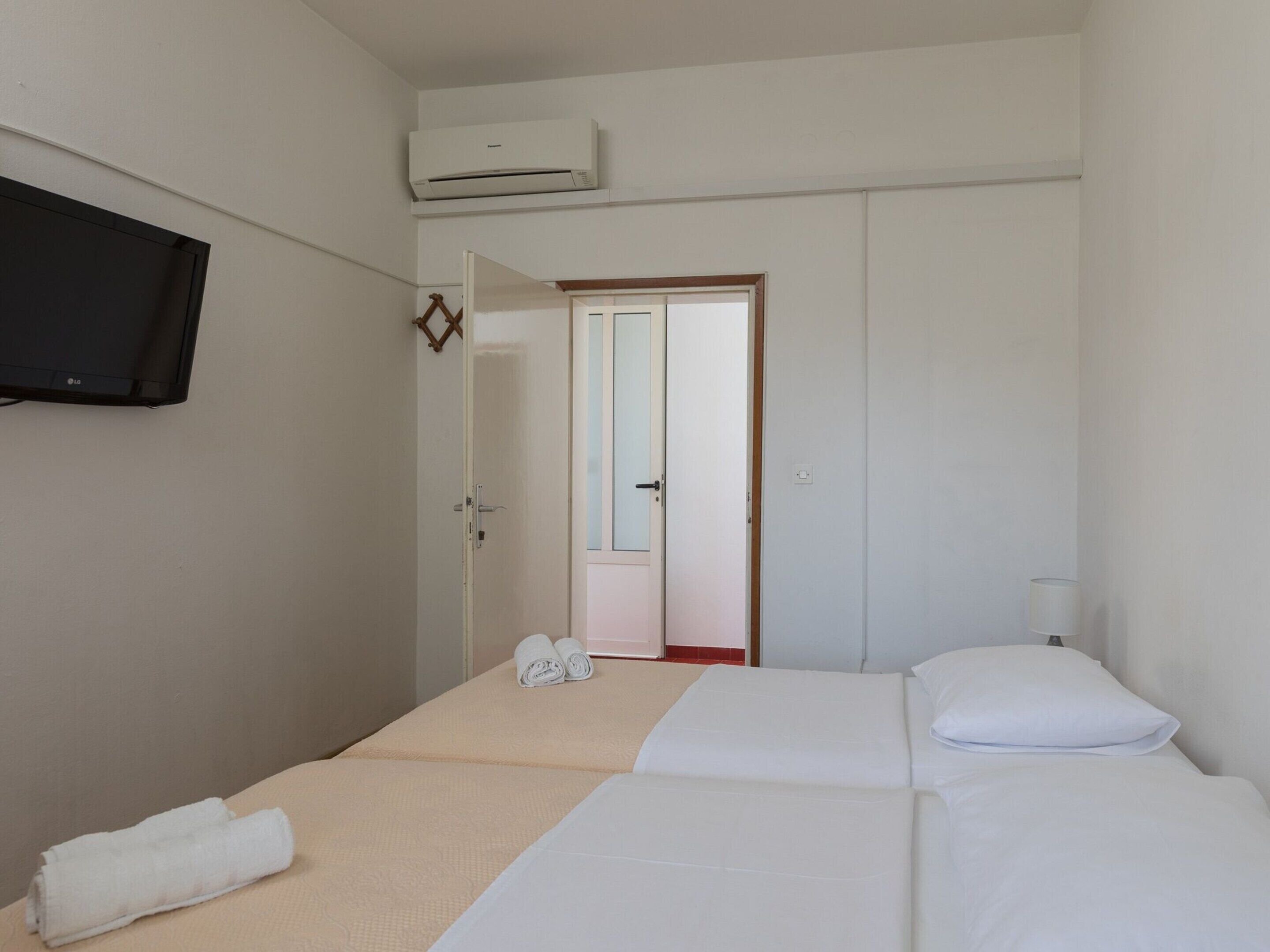 Quarto de hotel com uma cama, uma TV fixada na parede e um aparelho de ar condicionado sobre a cama.