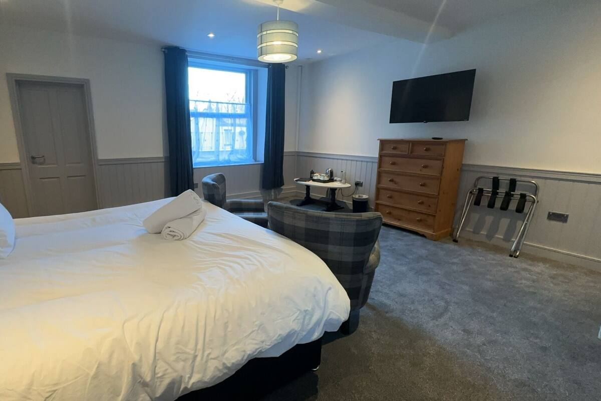 A hotel room with a large bed, a small round table, a TV mounted on the wall, and a dresser.