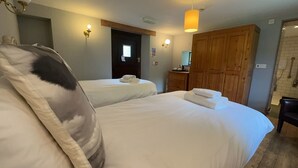 Une chambre d’hôtel avec deux lits, une armoire en bois, une porte et un petit bureau avec une lampe.