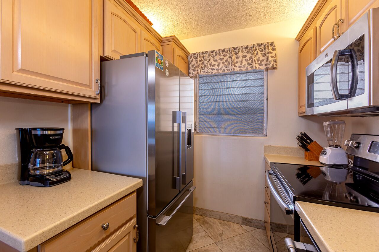 A compact kitchen with a stainless steel refrigerator, a coffee maker, a microwave, and a blender on the countertop.