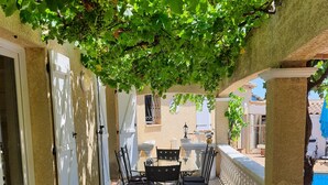 A covered patio area with a table and chairs, a pool in the background, and a stone wall.