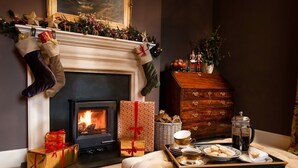 Ein gemütliches Wohnzimmer mit Kamin, Weihnachtssocken, Geschenken und einer Keksplatte.