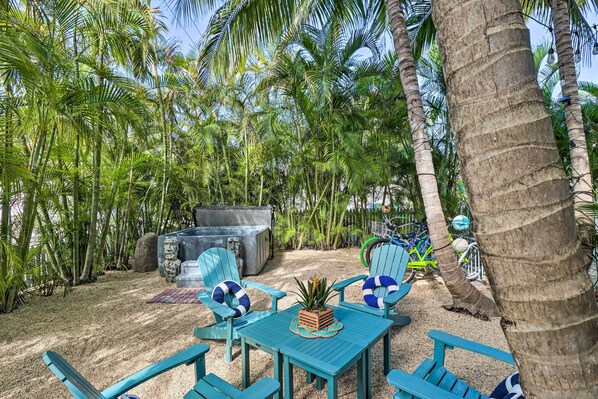 A tropical outdoor seating area with a table and chairs, surrounded by palm trees and a hot tub.