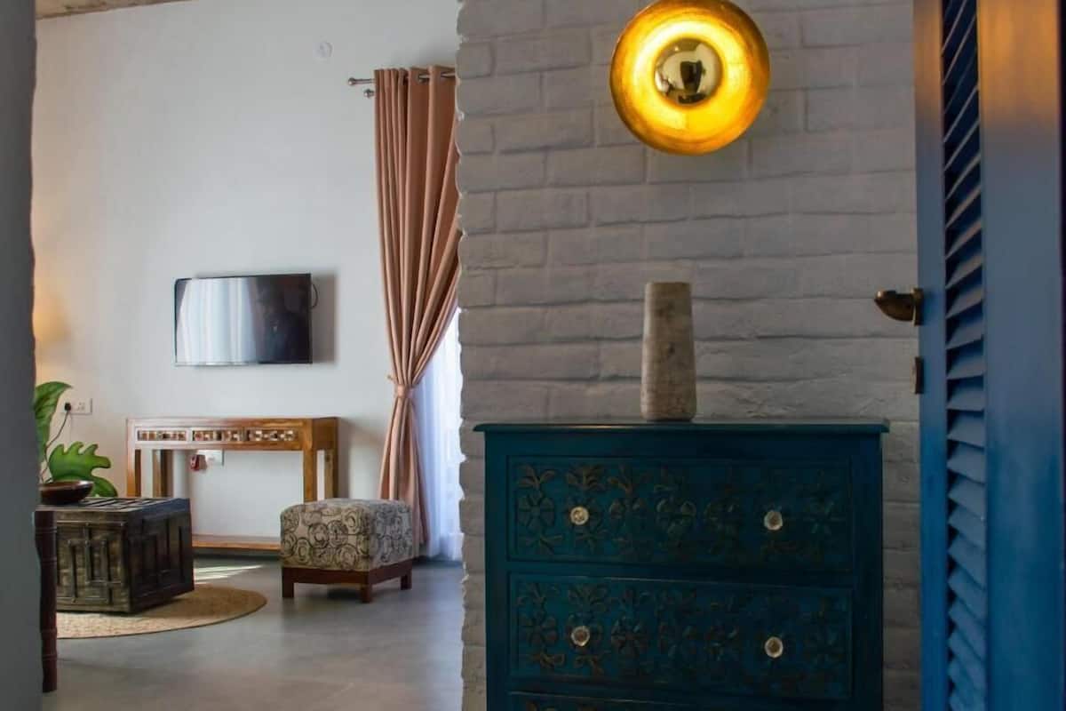 Une pièce comprenant une commode bleue, un meuble en bois, un pouf à motifs, une plante en pot et un luminaire fixé au mur.