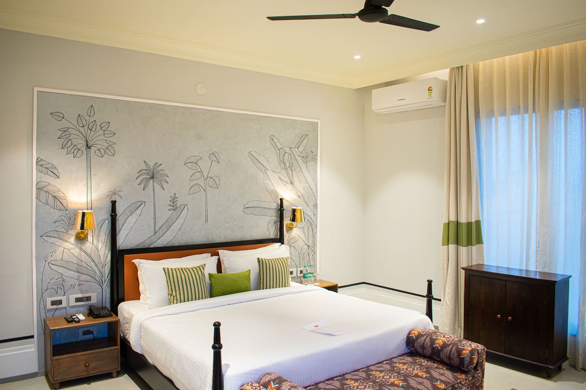 Une chambre d’hôtel avec un grand lit, une table de chevet avec un téléphone et une lampe, une armoire en bois et un ventilateur de plafond.