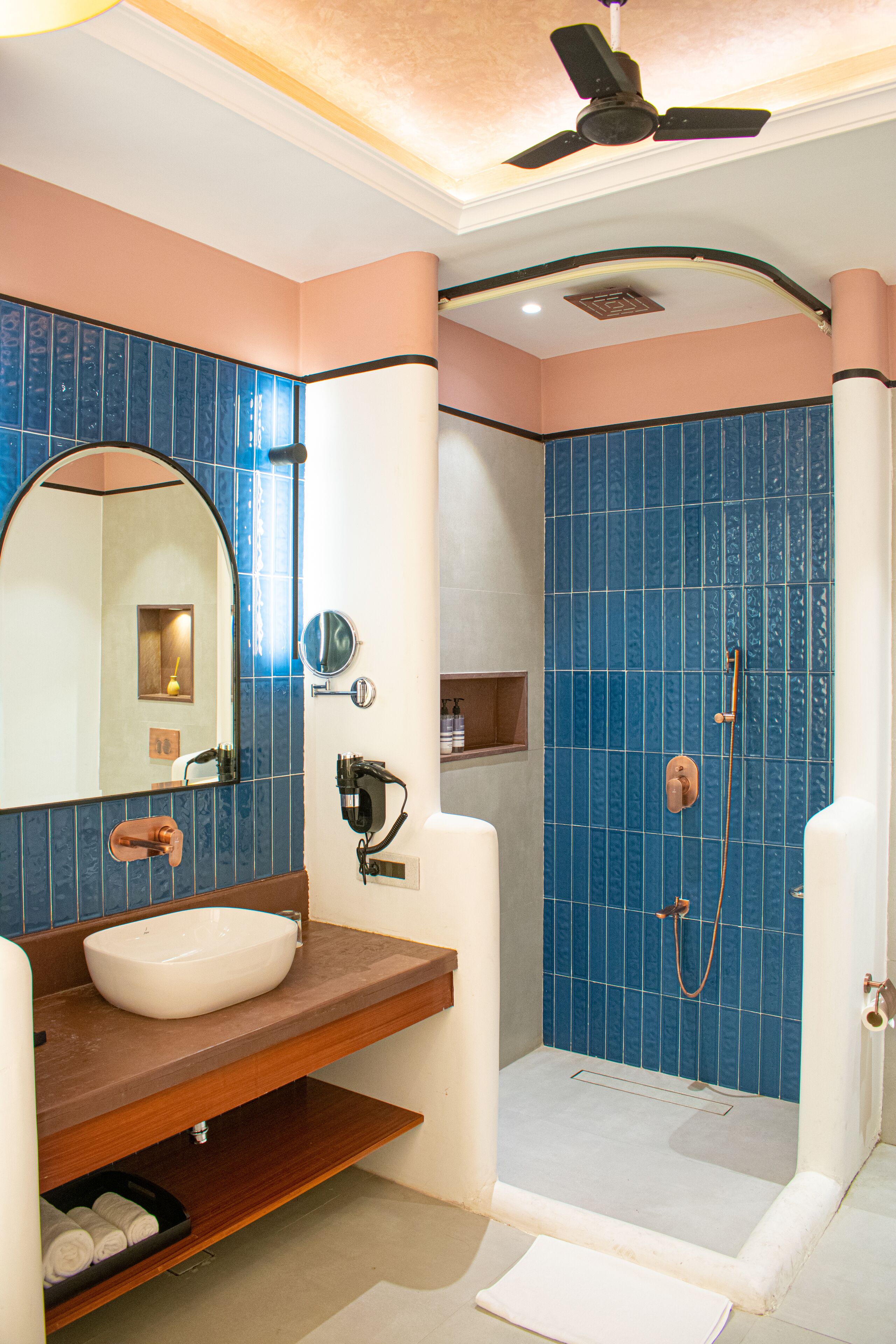 A bathroom with a white sink, a mirror, a shower with blue tiles, and a ceiling fan.
