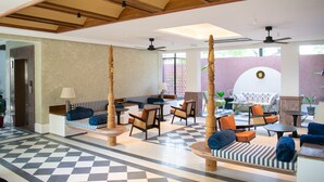 Een ruime lobby met een zwart-wit schachbordvloer, diverse zithoeken met banken en stoelen, en een plafondventilator.