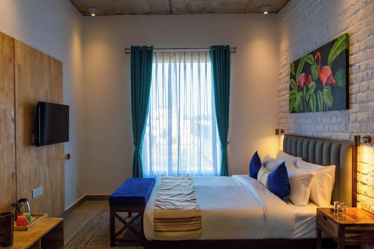 Une chambre d’hôtel avec un lit, un banc, une télévision et un tableau au mur.