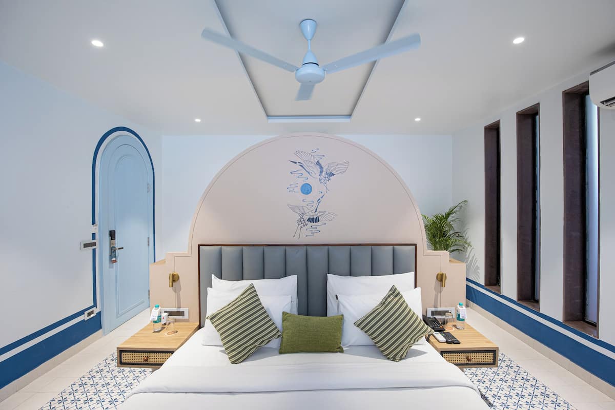 Une chambre d’hôtel moderne avec un grand lit, un ventilateur de plafond, une œuvre d’art décorative au mur et une plante en pot.