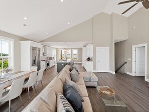 A spacious living area with a large sofa, dining table, and kitchen in the background. - Cabin by the Sea #138 - Private Pool, Second Row Oceanfront & Sound Views! (North Topsail Beach)