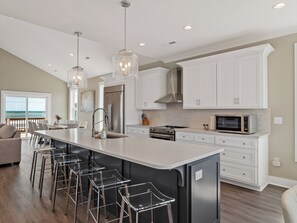 A modern kitchen with a large island, stainless steel appliances, and bar stools. - Cabin by the Sea #138 - Private Pool, Second Row Oceanfront & Sound Views! (North Topsail Beach)