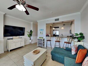 A living room with a television, white cabinets, a ceiling fan, and a teal sofa with orange pillows. - Windemere #1104 | Pool + Beach Access & Views! (Perdido Key)