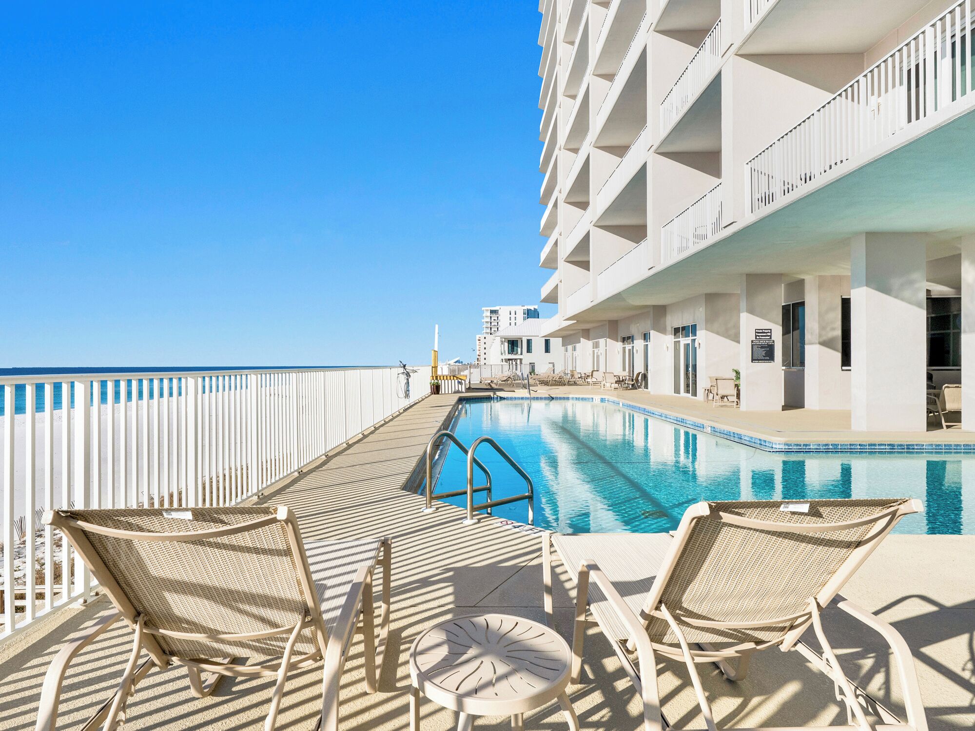 A pool area with lounge chairs and a view of the ocean.