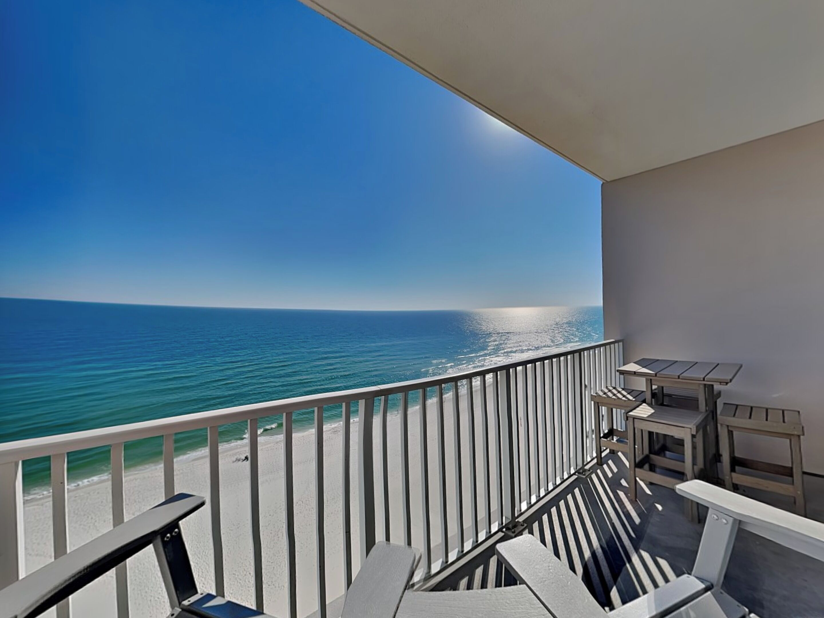A balcony with a view of the ocean, a railing, and a table with chairs.