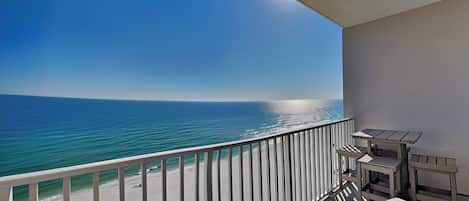 Uma varanda com vista para o mar, corrimão e uma mesa com cadeiras.