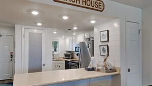 A modern kitchen with white cabinets, a stainless steel refrigerator, and a bar area with stools. - Palm View | Serene Views, Cozy Interior, Near Area Fun! (Gulf Shores)