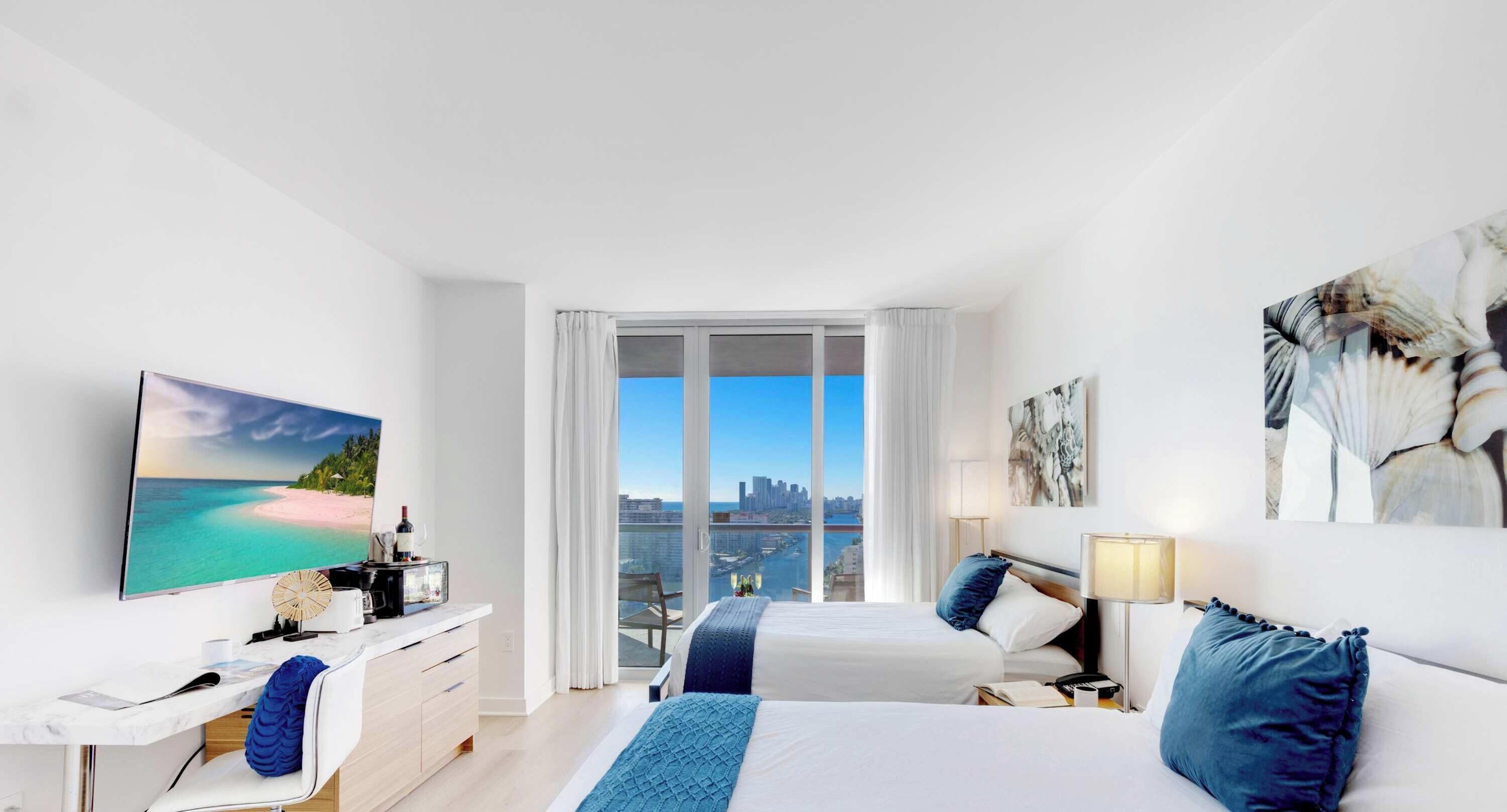 A modern hotel room with a large bed, a desk, a chair, and a view of the city.