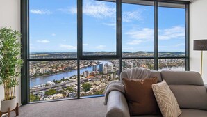 A modern living room with a large window overlooking a cityscape and river. - Luxury 4 Bedroom Sub Penthouse with Ocean Views (Brisbane City)