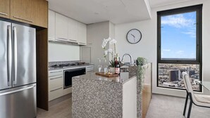 A modern kitchen with a stainless steel refrigerator, a built-in oven, and a granite countertop island. - Luxury 4 Bedroom Sub Penthouse with Ocean Views (Brisbane City)