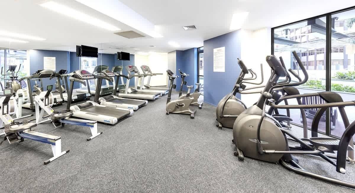 Un gimnasio con cintas de correr, elípticas y bicicletas estáticas dispuestas en filas.