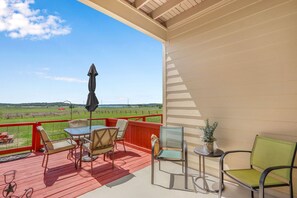 Ein überdachter Außenbereich mit Tisch und Stühlen, einem Blumentopf und Blick auf ein grünes Feld.