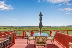 Eine rote Terrasse mit Glastisch und Stühlen, einem Sonnenschirm und Blick auf ein grünes Feld und die Ferne.
