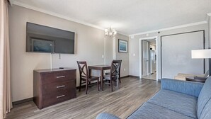 A modern living room with a sofa, a TV, a dining table with chairs, and a dresser. - Ocean Front 1BR - Caravelle 1036 (Myrtle Beach)