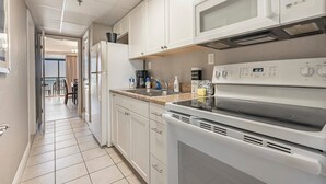 A modern kitchen with white cabinets, a microwave, a stove, and a coffee maker. - Ocean Front 1BR - Caravelle 1036 (Myrtle Beach)