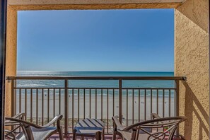 Een balkon met uitzicht op het strand, metalen hekwerk en twee stoelen.