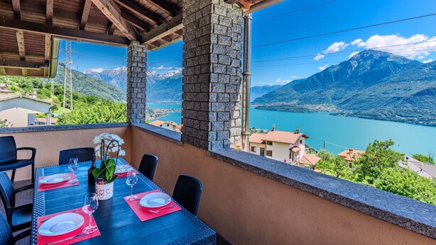 Una terraza con mesa lista para comer, con vista a un lago y montañas.
