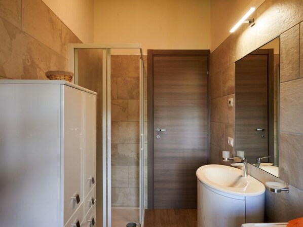 Un baño moderno con cabina de ducha de vidrio, un lavabo blanco y un espejo grande.