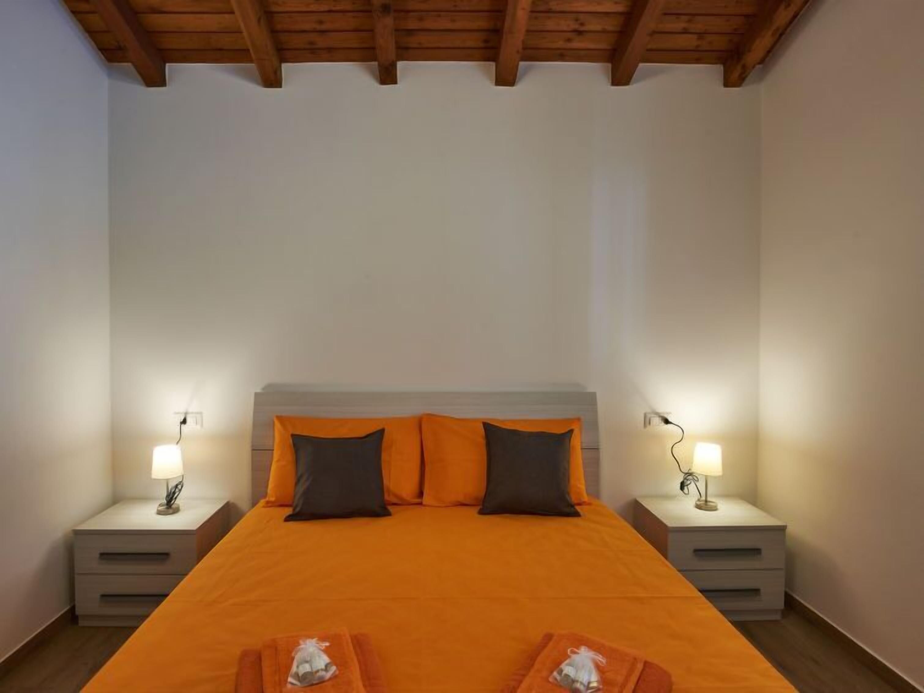 Un dormitori amb un llit gran, dues taules de nit i un sostre de fusta.
