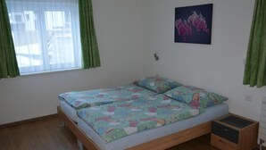 A bedroom with a wooden bed, green curtains, a window, and a wall-mounted picture.