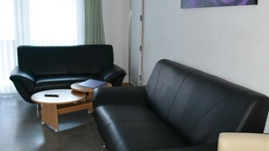 A modern living room with a black leather sofa, a beige armchair, and a small wooden coffee table. A large abstract painting adorns the wall.