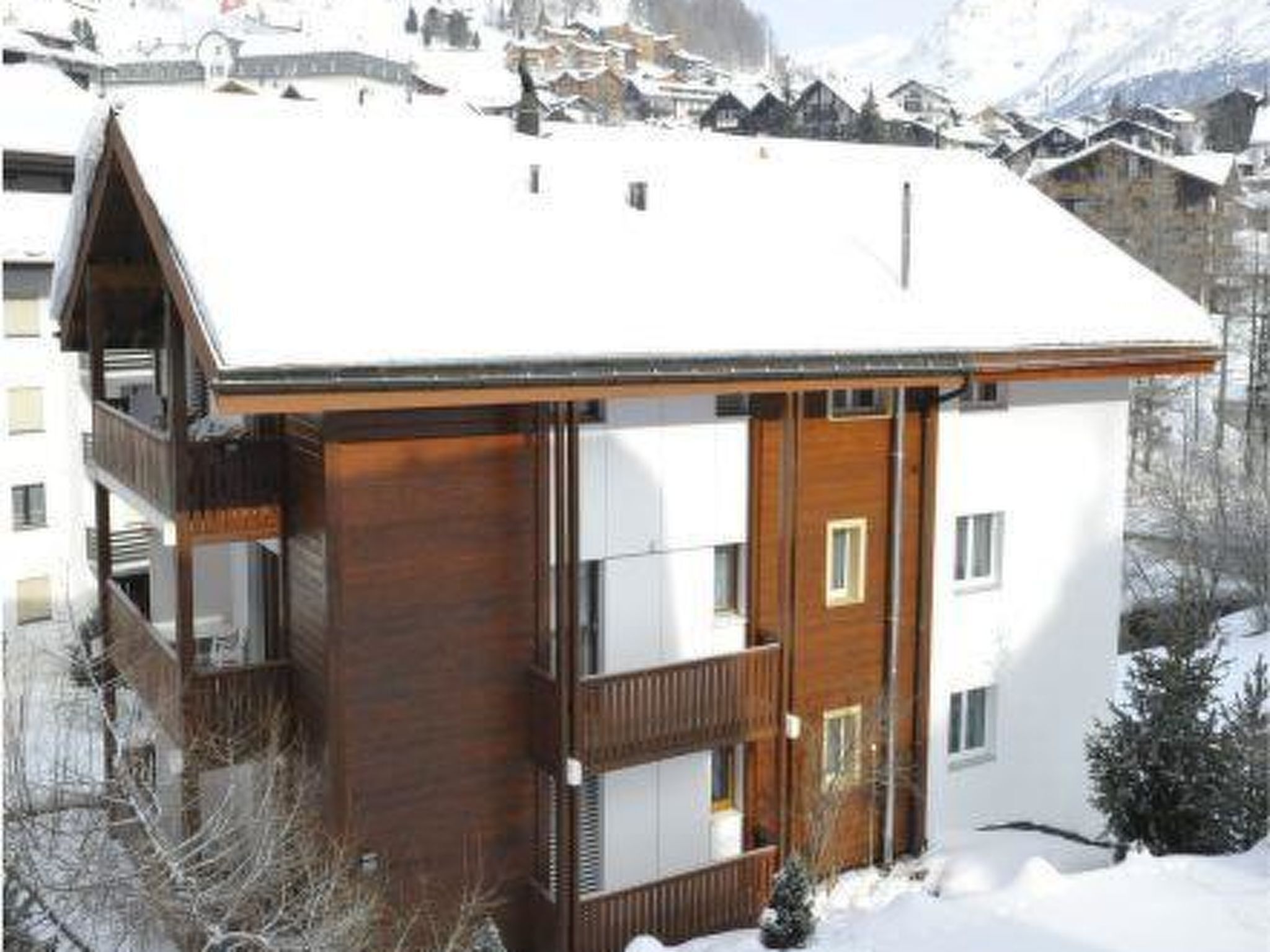 Um edifício com várias andares, fachada de madeira e varandas, rodeado por montanhas cobertas de neve.