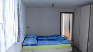 A single bed with a green mattress and blue bedding, a wardrobe, and a door leading to another room. - Amasaas by Interhome (Saas-Fee)
