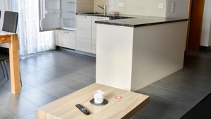 Et moderne køkken med en central ø, lyse skabe og et spiseområde med et bord.