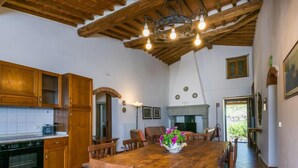 A rustic kitchen with wooden cabinets, a dining table with chairs, a chandelier, and a fireplace.
